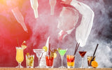Man throwing a flair bottle behind a table of cocktails