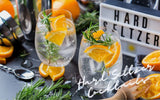 2 Glasses of hard seltzer cocktails with orange wedge garnish