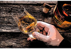 Hand holding a whiskey in a glass for tasting on a wooden background